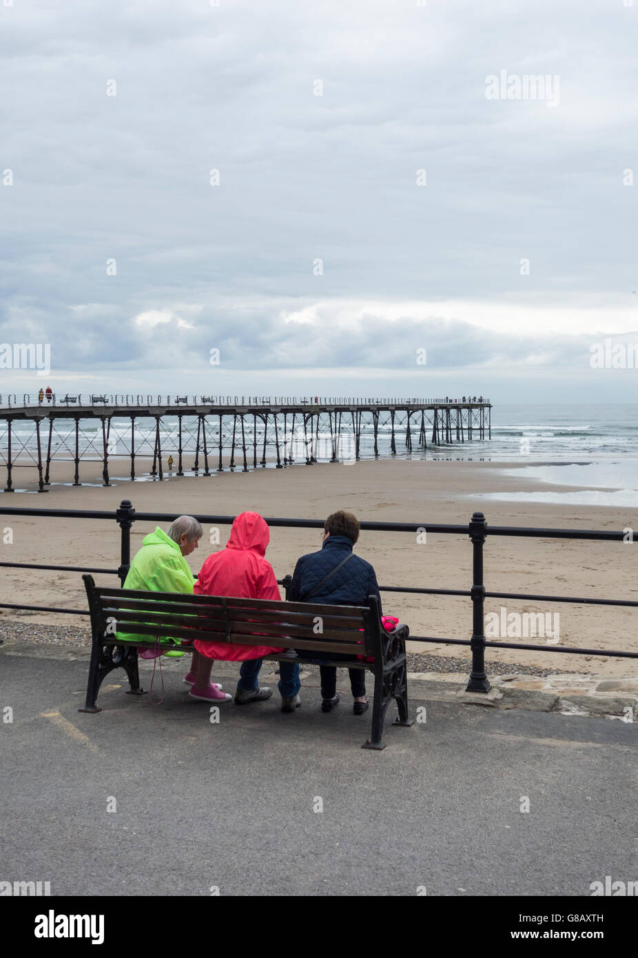 Rear view of 3 mature women sitting on bench near Saltburn`s Victorian pier. Saltburn by the sea, North Yorkshire, England. UK Stock Photo